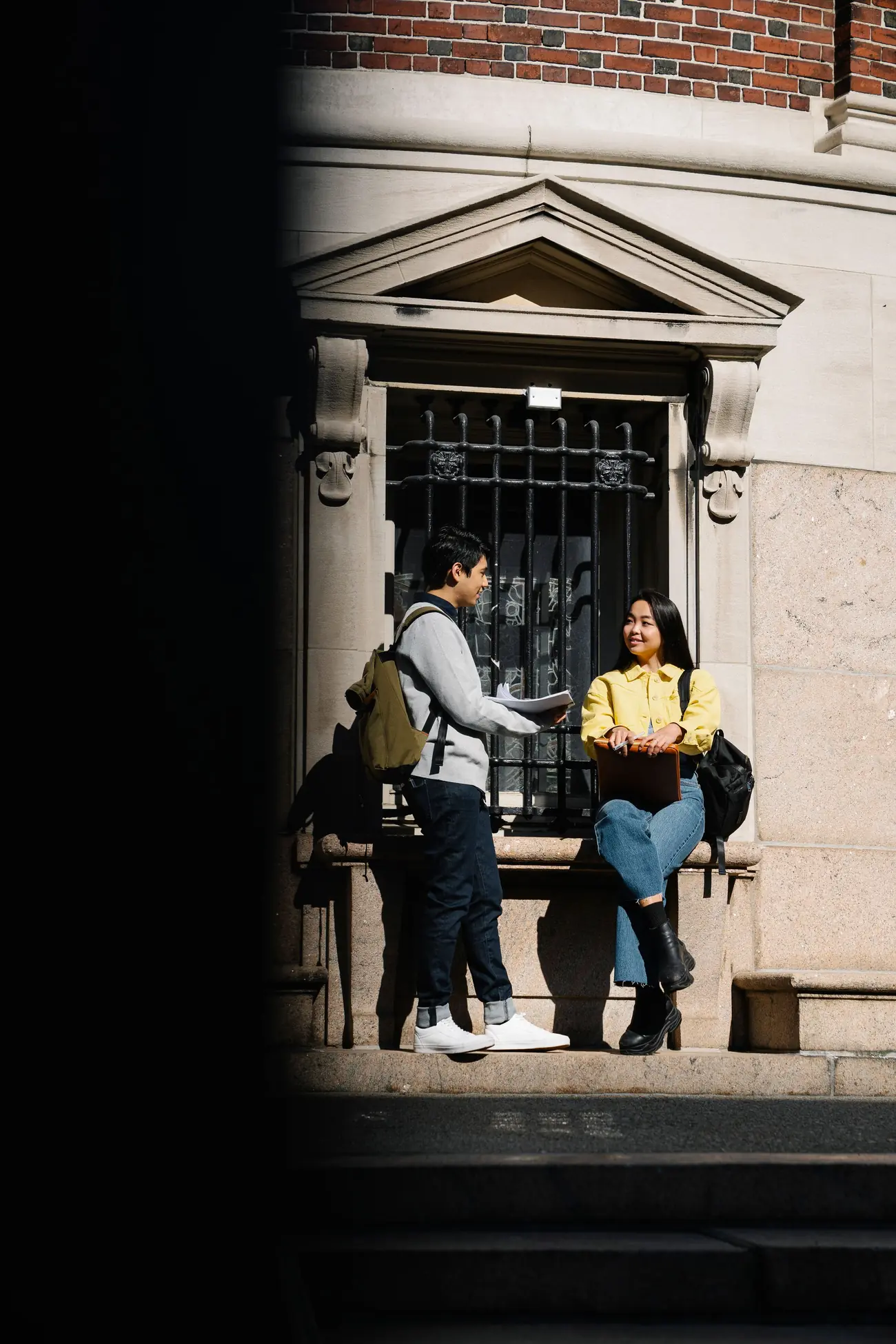 Two students talking in the sunlit doorway of an old stone building