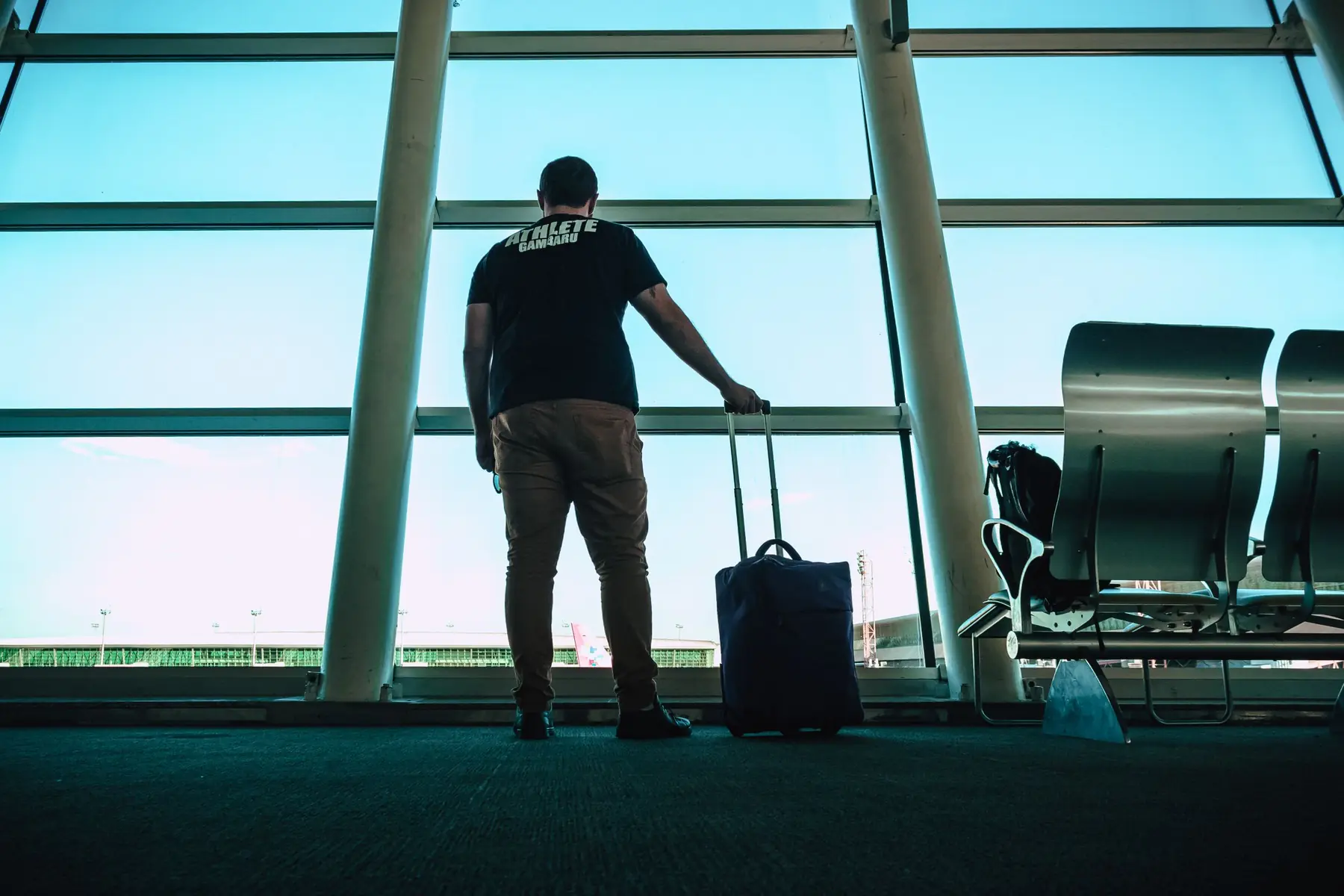 A student with a suitcase looking out at planes through a tall airport window
