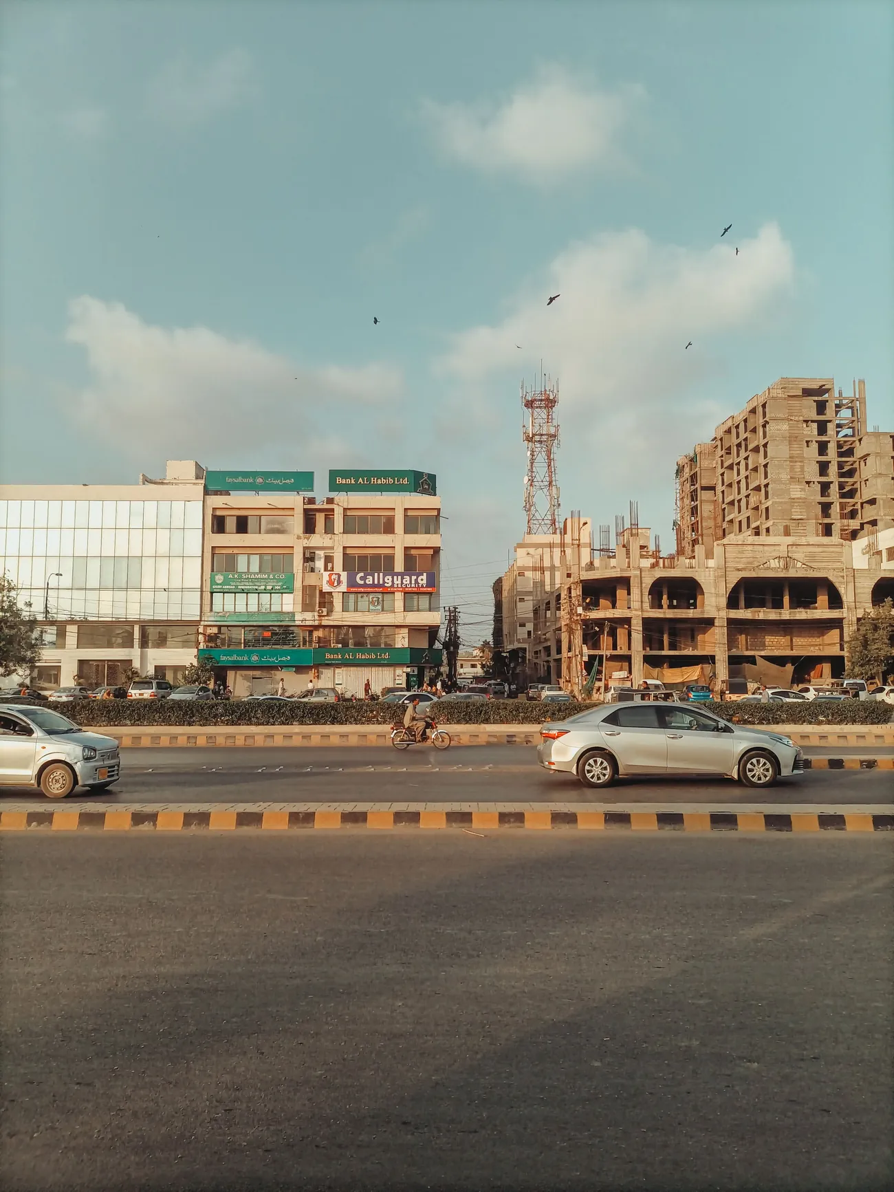 A wide Karachi road lined with shops and apartment blocks under a clear sky