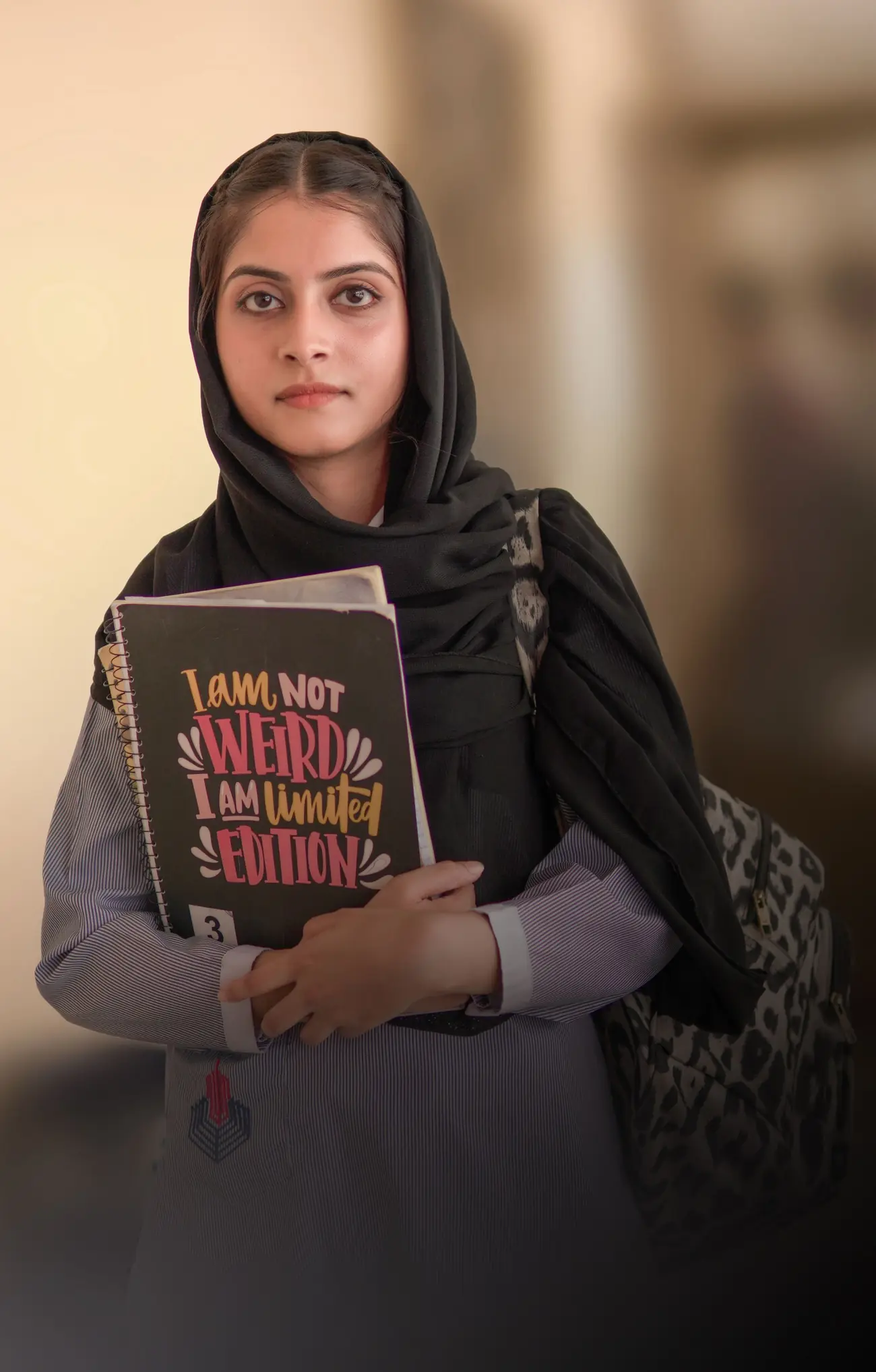 A student in a headscarf holding her notebook close