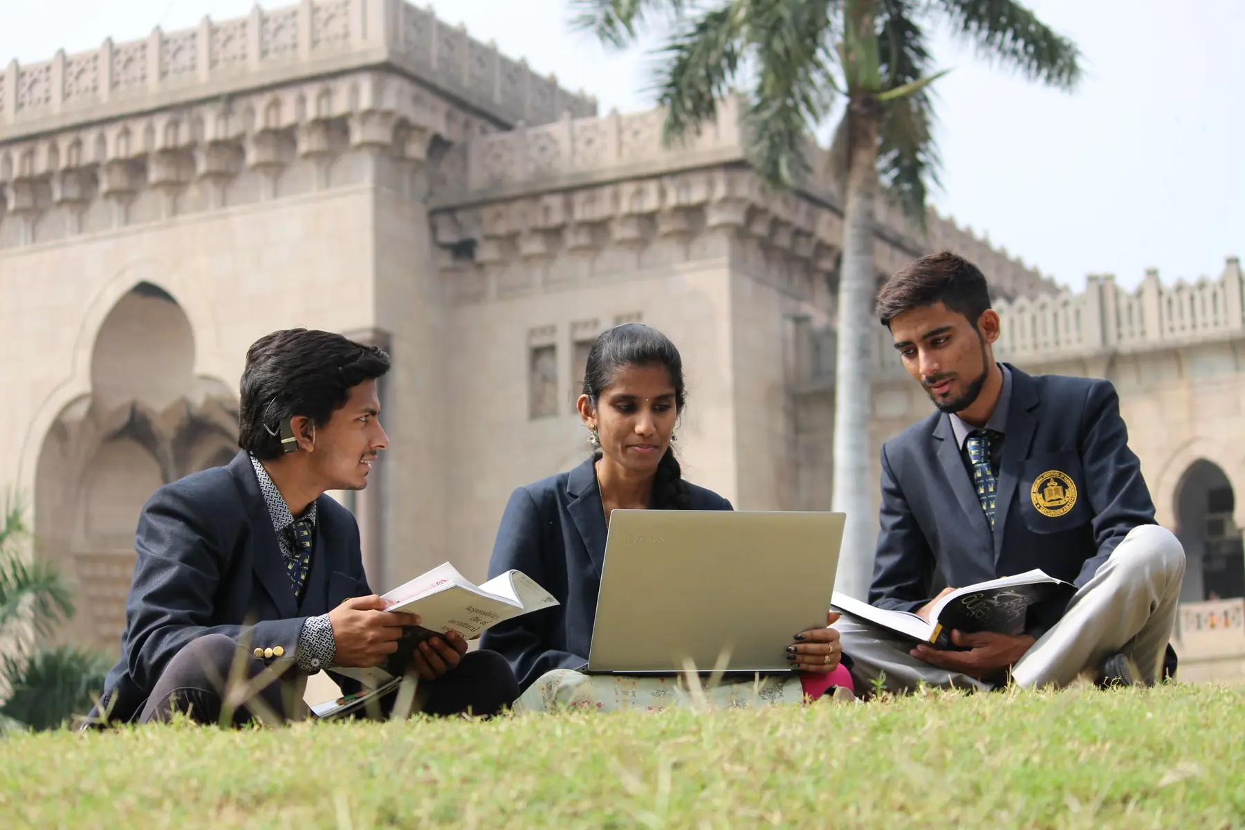 Students in school blazers studying together on a campus lawn with a laptop