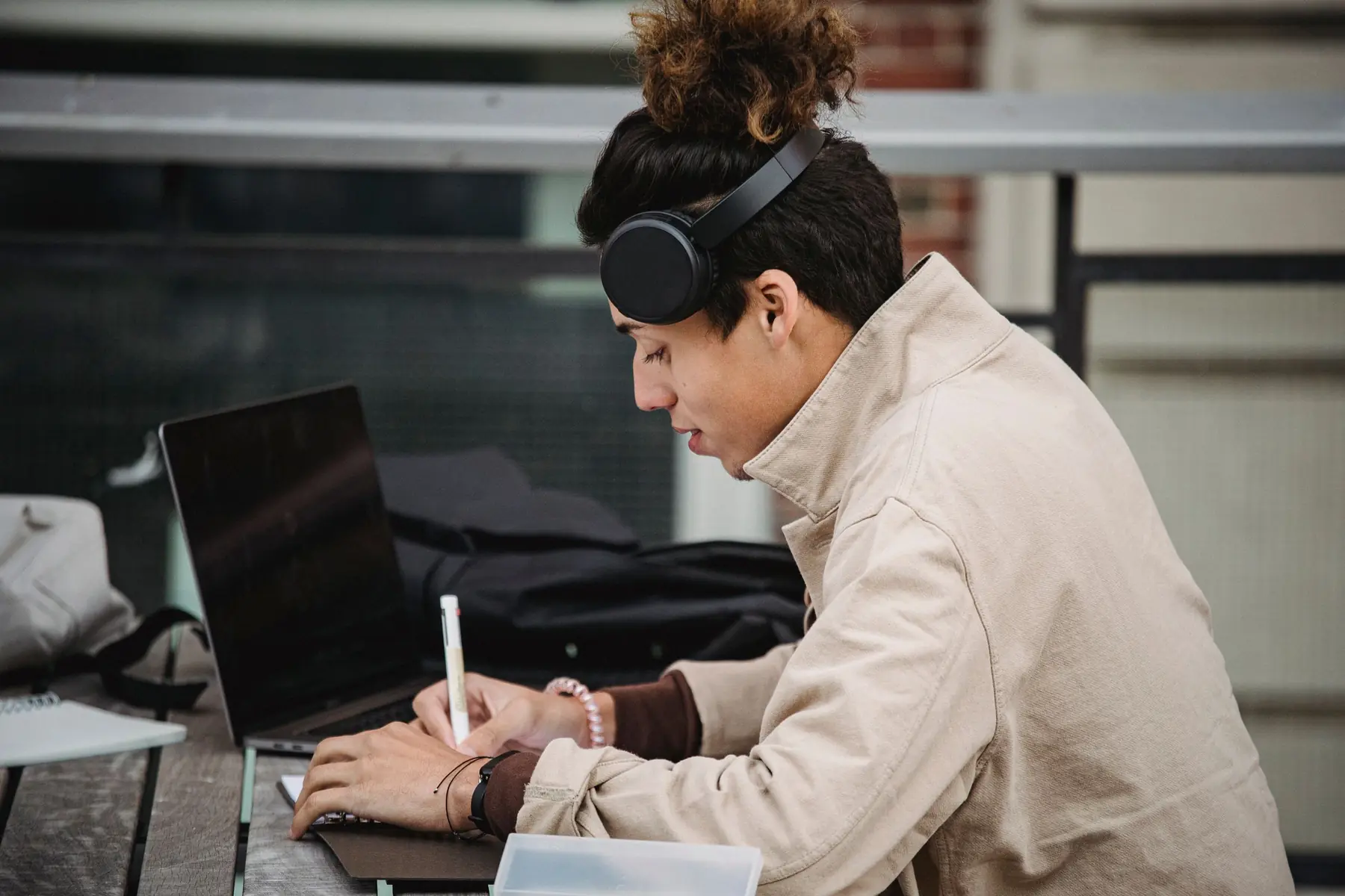 A young man in headphones taking notes beside his laptop