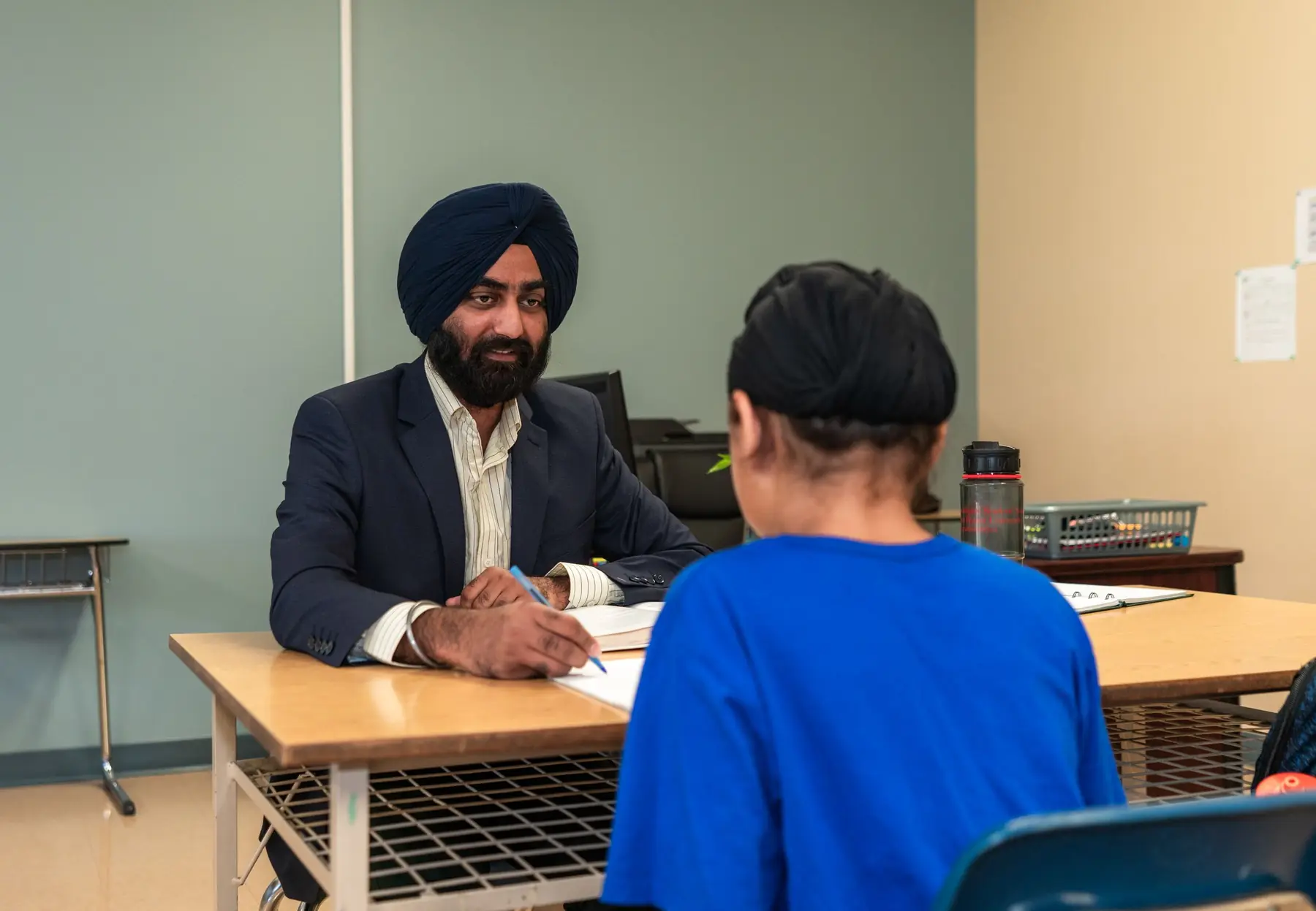 A teacher and a student in a one to one conversation across a classroom desk