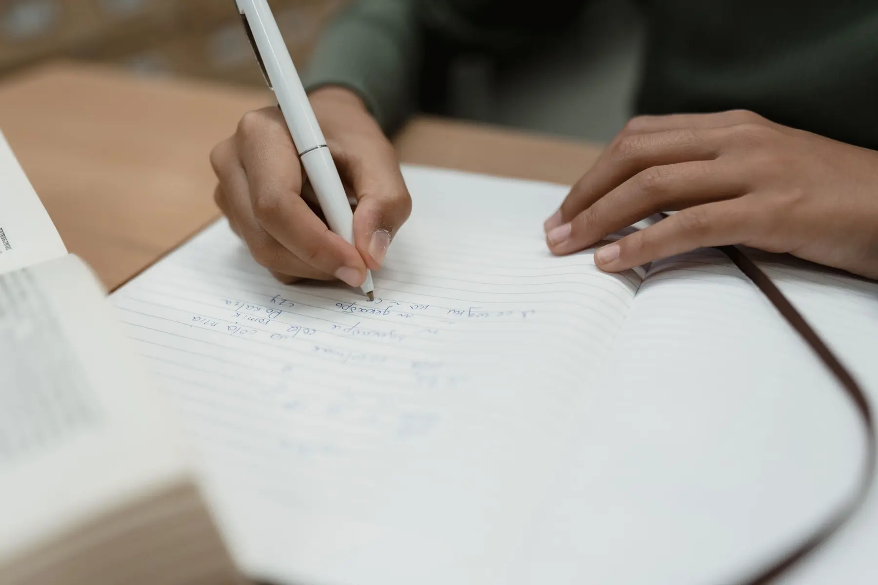 A hand writing in a lined notebook with a white pen