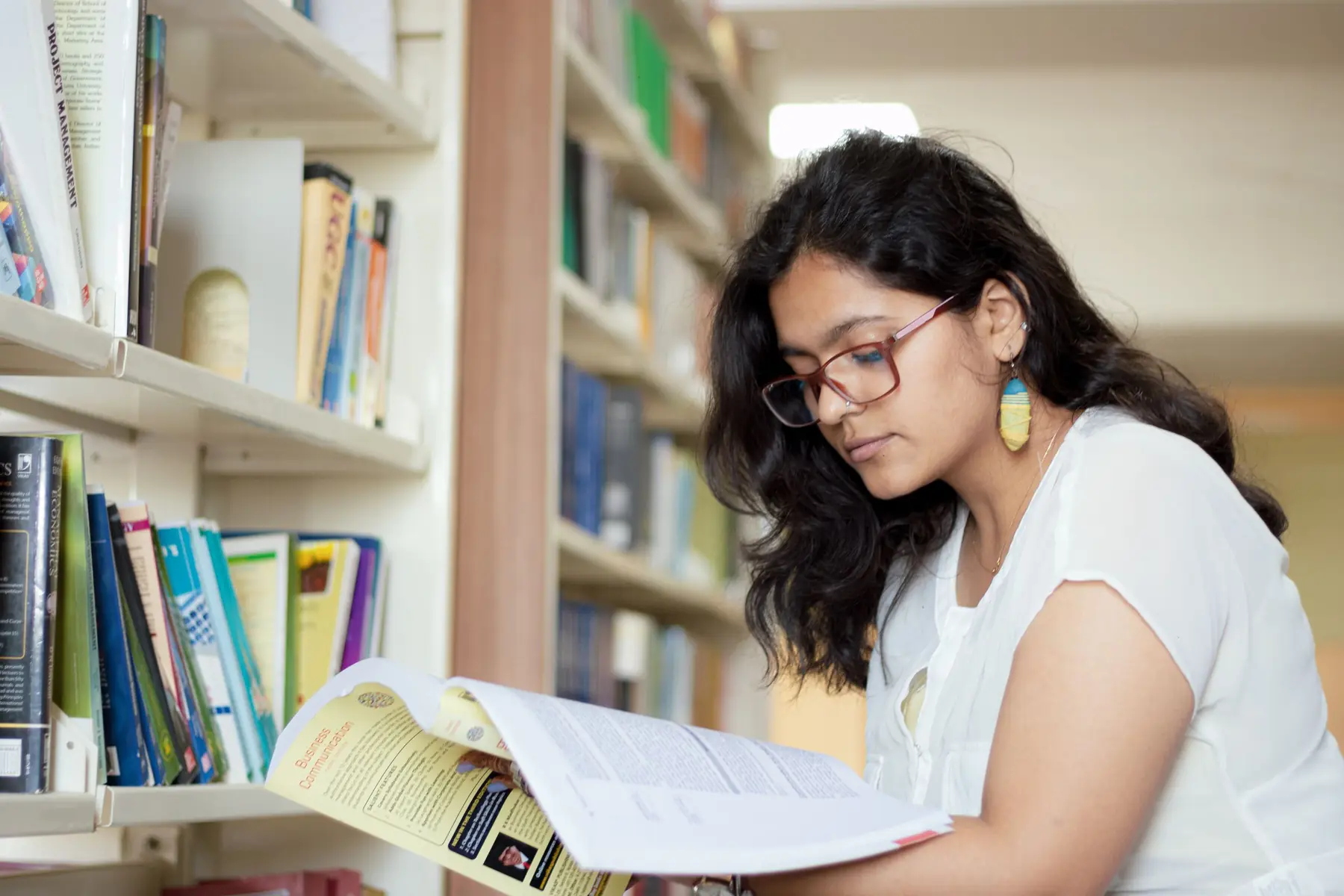 A smiling student reading a book between library shelves