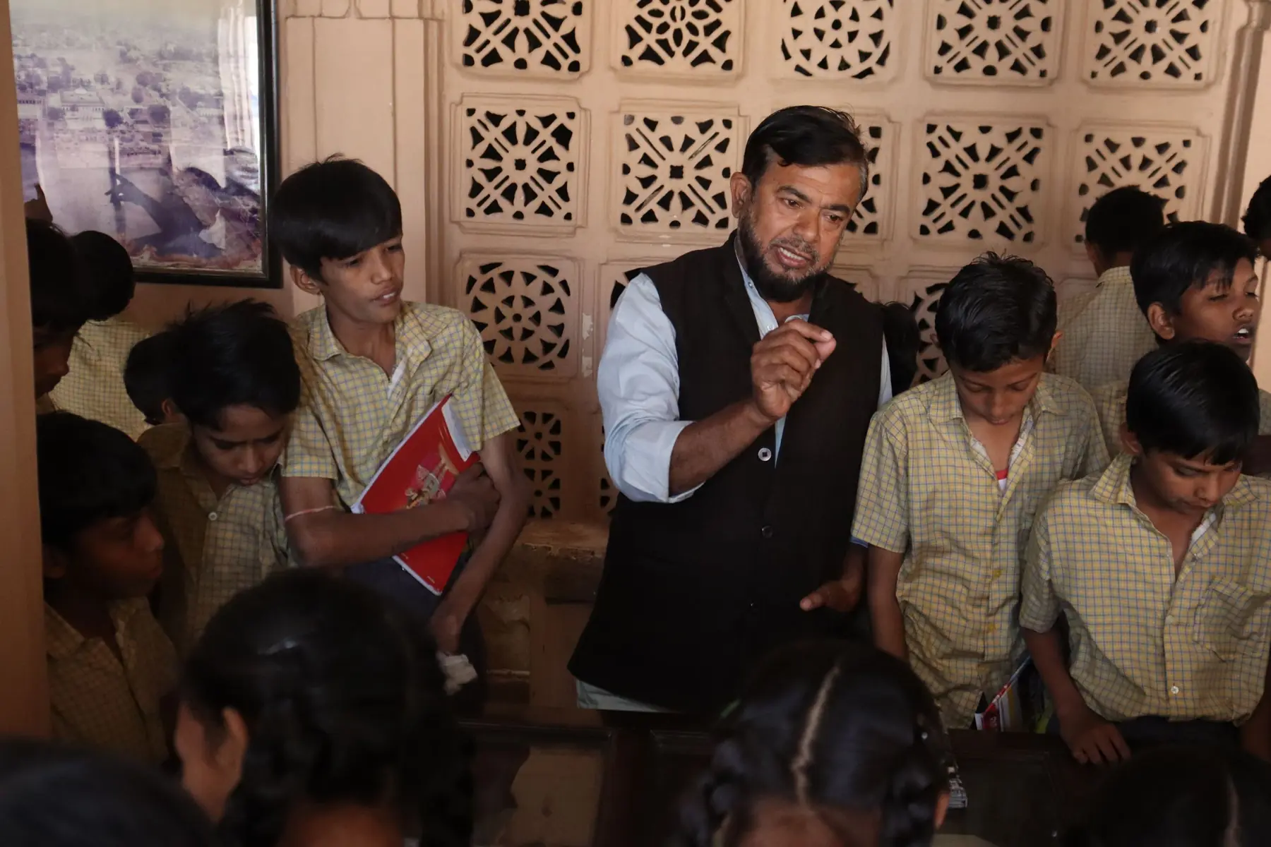 A teacher talking with a group of students in a classroom with carved wooden screens